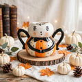 Spider Mug by Johanna Parker Design for Transpac styled with cream pumpkins, autumn leaves, pinecones, and vintage books
